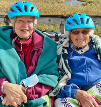 Two residents sitting on a custom bicycle at Three Pillars.